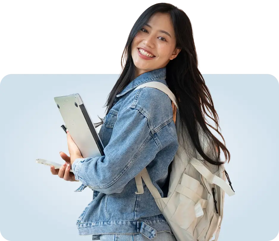 Smiling young Asian female college student wearing a denim jacket and backpack, holding a laptop and smartphone