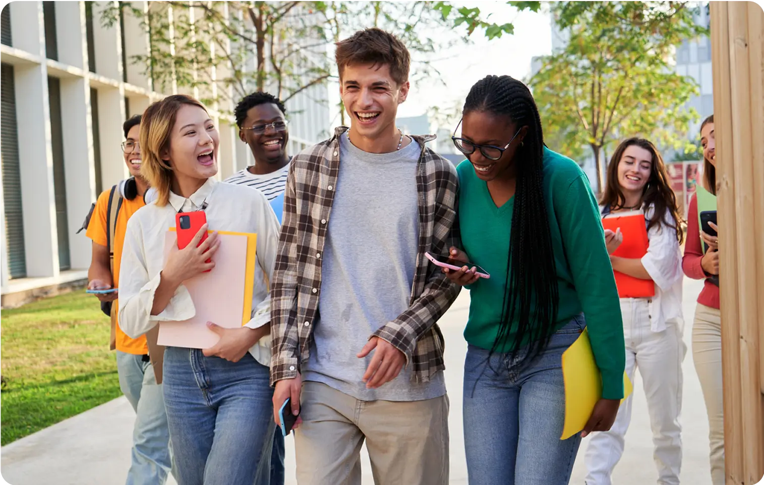 Diverse group of happy college students walking outdoors on a sunny day, laughing and carrying books and folders