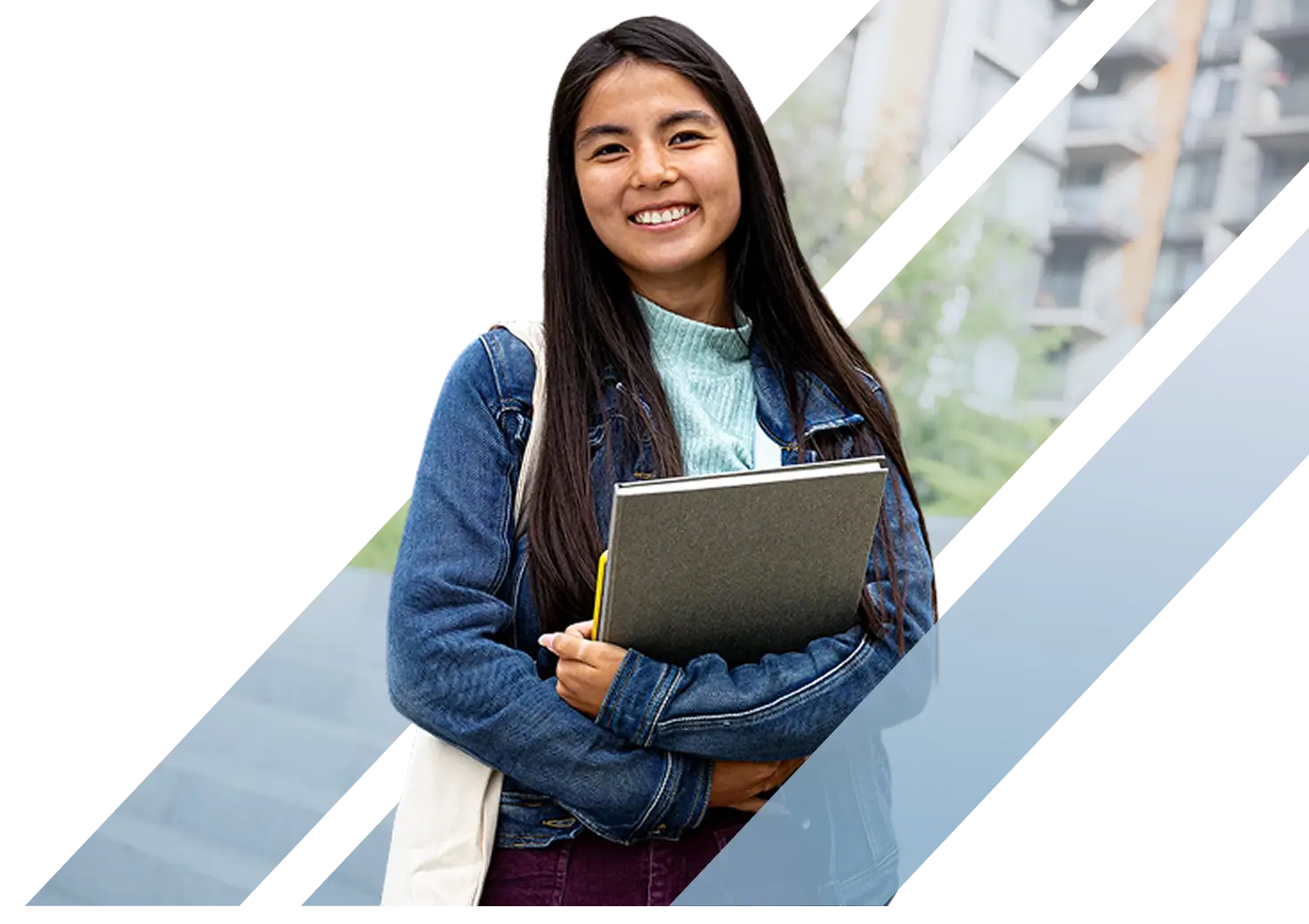 A smiling young female Asian college student holding a notebook and wearing a denim jacket on campus