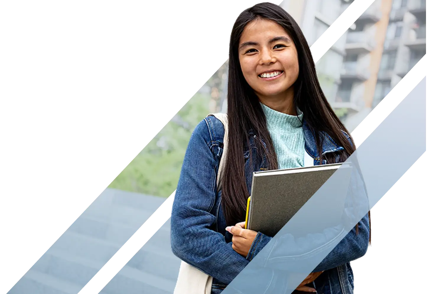 A smiling young female Asian college student holding a notebook and wearing a denim jacket on campus