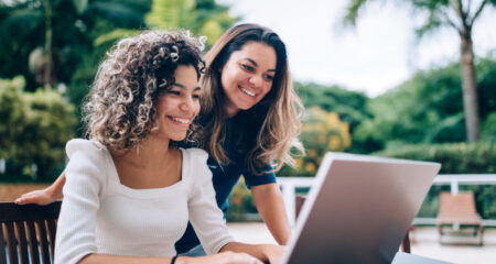 Mother and daughter using laptop at swimming pool area