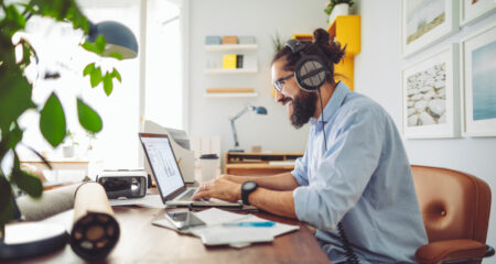 A man with headphones on typing at a laptop while sitting at a desk