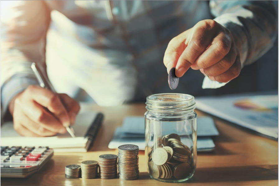 a man putting coins in a jar and writing on a notepad