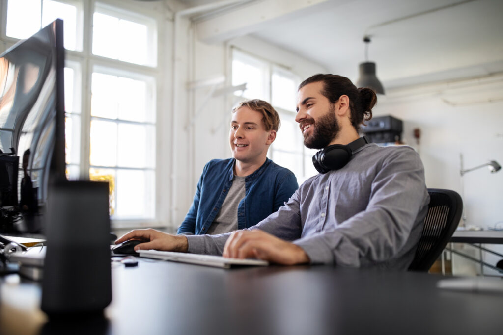 Two business people sitting at desk and working on computer in office. Software engineers working together at their desk.