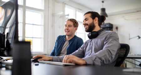 Two business people sitting at desk and working on computer in office. Software engineers working together at their desk.