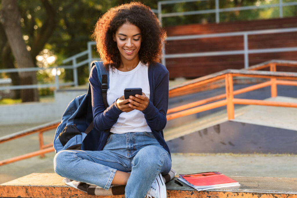 Young woman sitting outdoors in park using mobile phone.