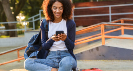 Young woman sitting outdoors in park using mobile phone.