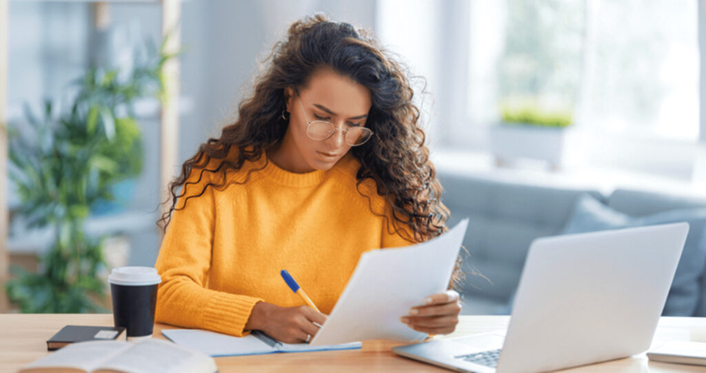 Woman taking notes fro mcomputer and paper