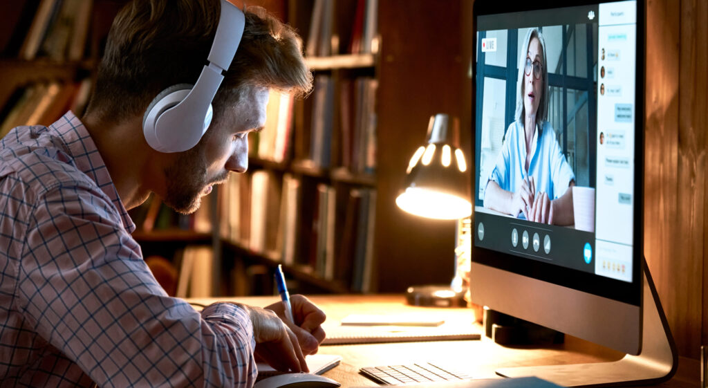 male student with headphones takes notes during an online college class