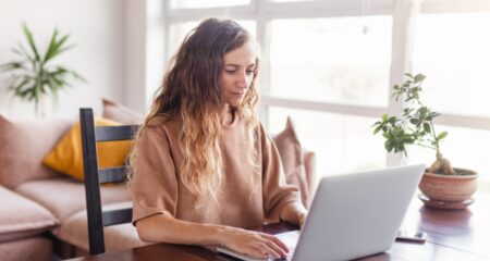 Young woman reads student loan news on her laptop at the kitchen table