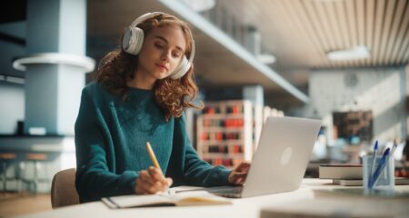 A female graduate student wearing headphones does homework in a college library