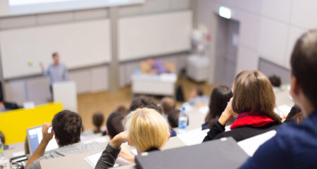 graduate students seated in lecture hall listen to professor and take notes