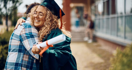 Happy graduate student in cap and gown celebrating with family after completing grad school