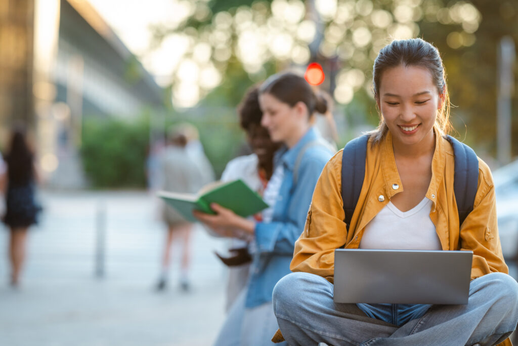 College student using a laptop outdoors while looking to improve their private student loan application.